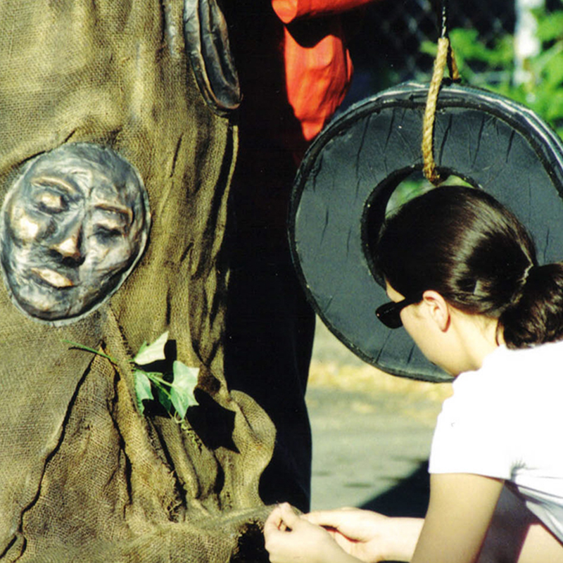 Youth sewing a community tree made out of burlap and paper-mashe diverse faces