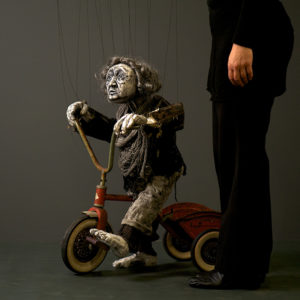 Old Woman marionette riding a rusted red tricycle