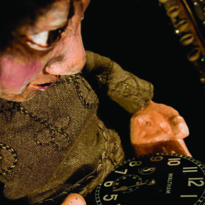 Close-up of puppet staring at a the hands of a pocket watch